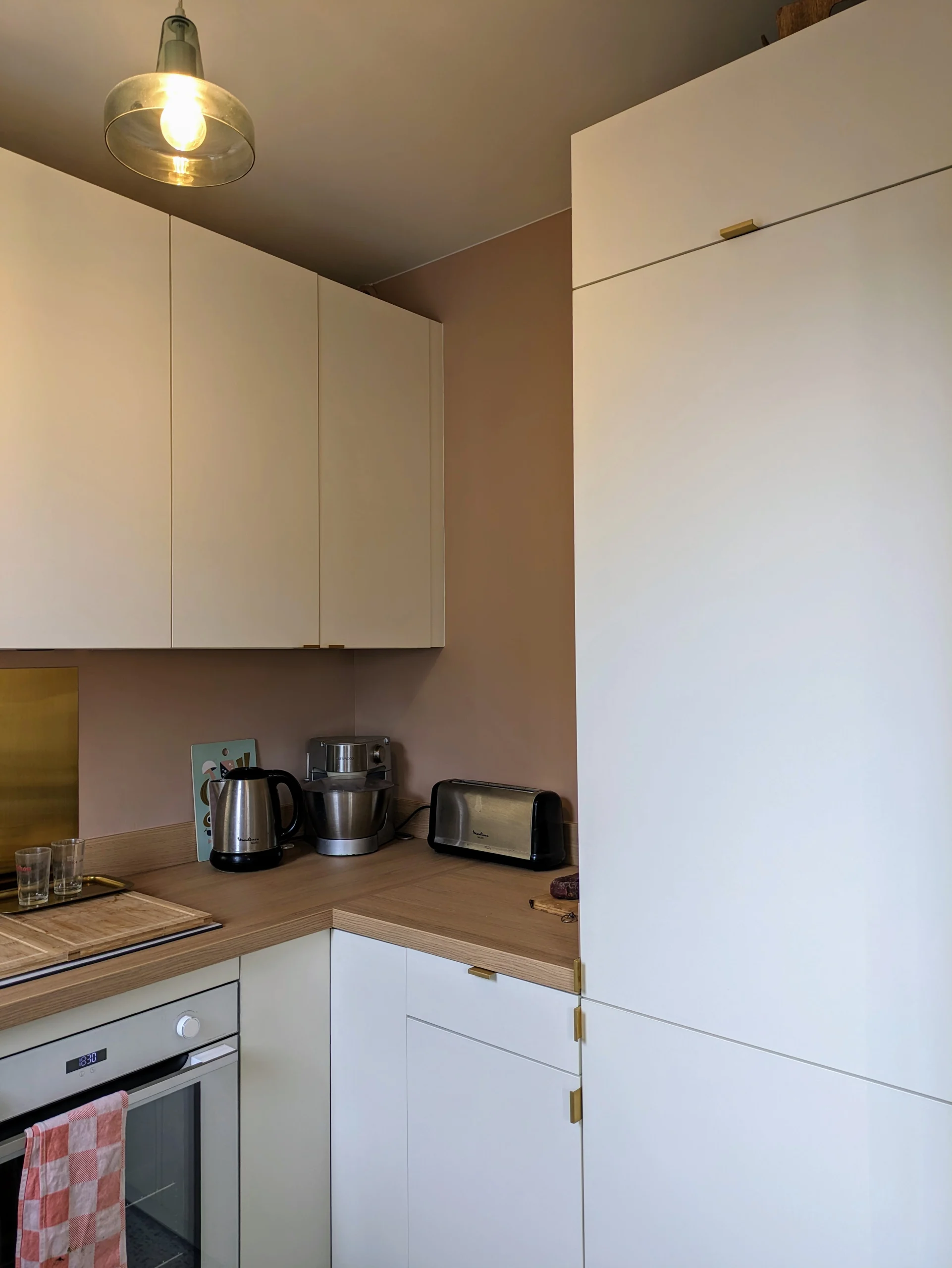 Projet de rénovation d'une cuisine sur-mesure - Vue d'un coin de la cuisine - murs rose Masquerade de Little Greene - Façade en laque mat blanc chaud - poignées en laiton - plan de travail chêne clair Vue d'un coin de la cuisine - murs rose Masquerade de Little Greene - Façade en laque mat blanc chaud - poignées en laiton - plan de travail chêne clair