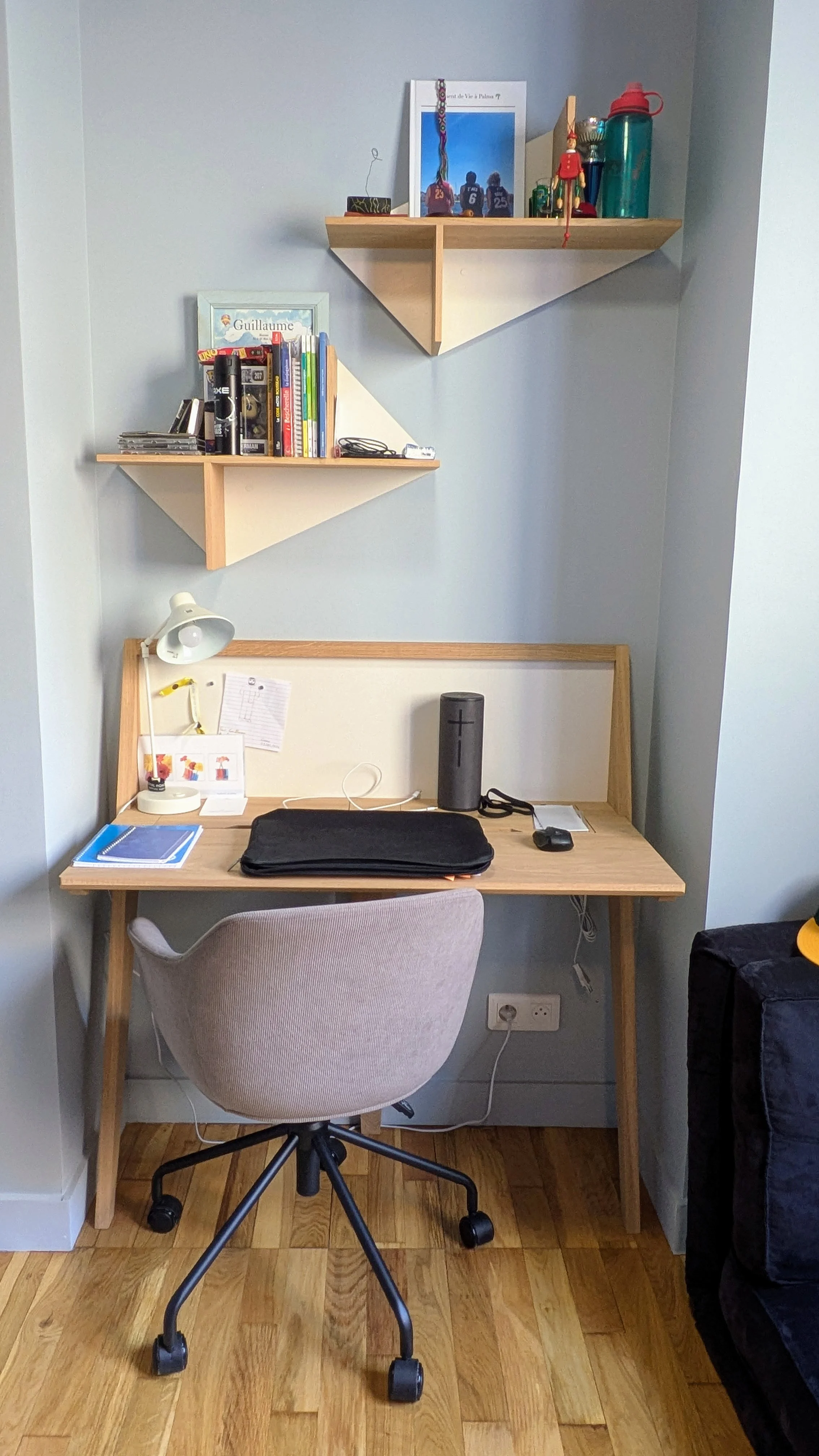 Un bureau sous pente pensé pour le confort et le style, mêlant mobilier en bois clair signé Drugeot Manufacture et mur habillé d’un papier peint graphique bleu nuit. Coin bureau aménagé sous pente avec mobilier Drugeot Manufacture et papier peint à motifs géométriques