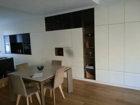 Cuisine ouverte moderne avec meubles blancs, éléments noirs brillants et table de salle à manger conviviale.